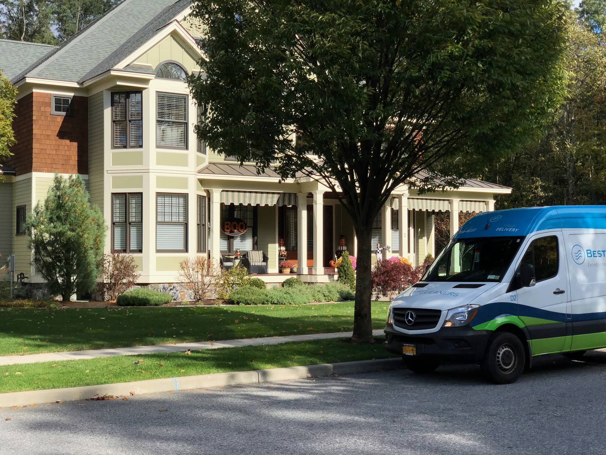 A blue and white service van is parked on the street in front of a two-story house with a porch and well-kept lawn.
