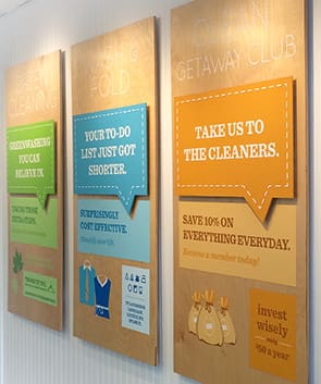 Three wooden wall signs advertise dry cleaning and laundry services, featuring promotional messages and icons in green, blue, and orange tones.