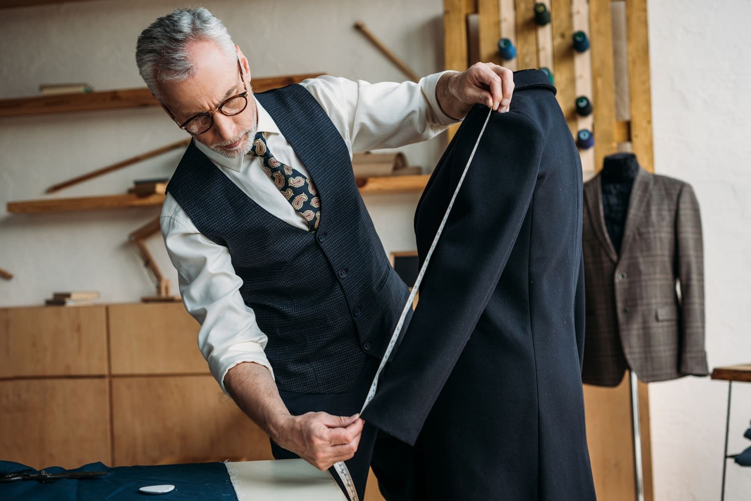 Tailoring specialist measuring sleeve length of a suit jacket in a professional alteration shop, emphasizing personalized clothing adjustments and expert tailoring services.