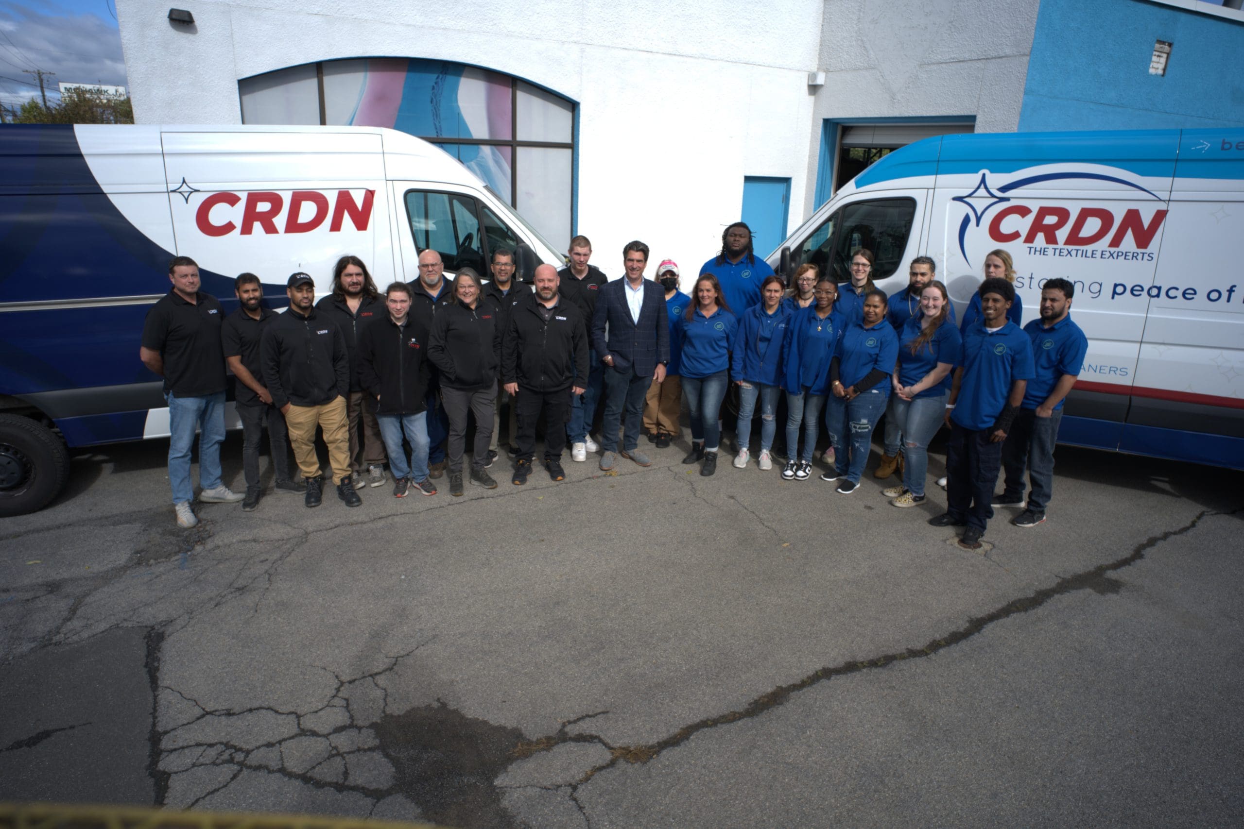 A group of people stands between two CRDN-branded vans outside a building, posing for a group photo.