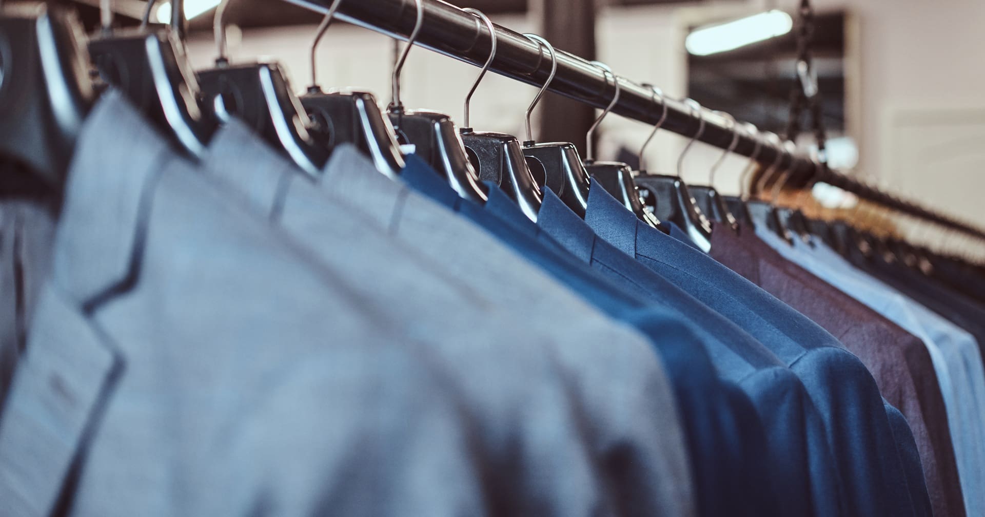 A row of blue and gray suits, freshly pressed by a Dry Cleaner New York, hang on black hangers on a clothing rack in a store.