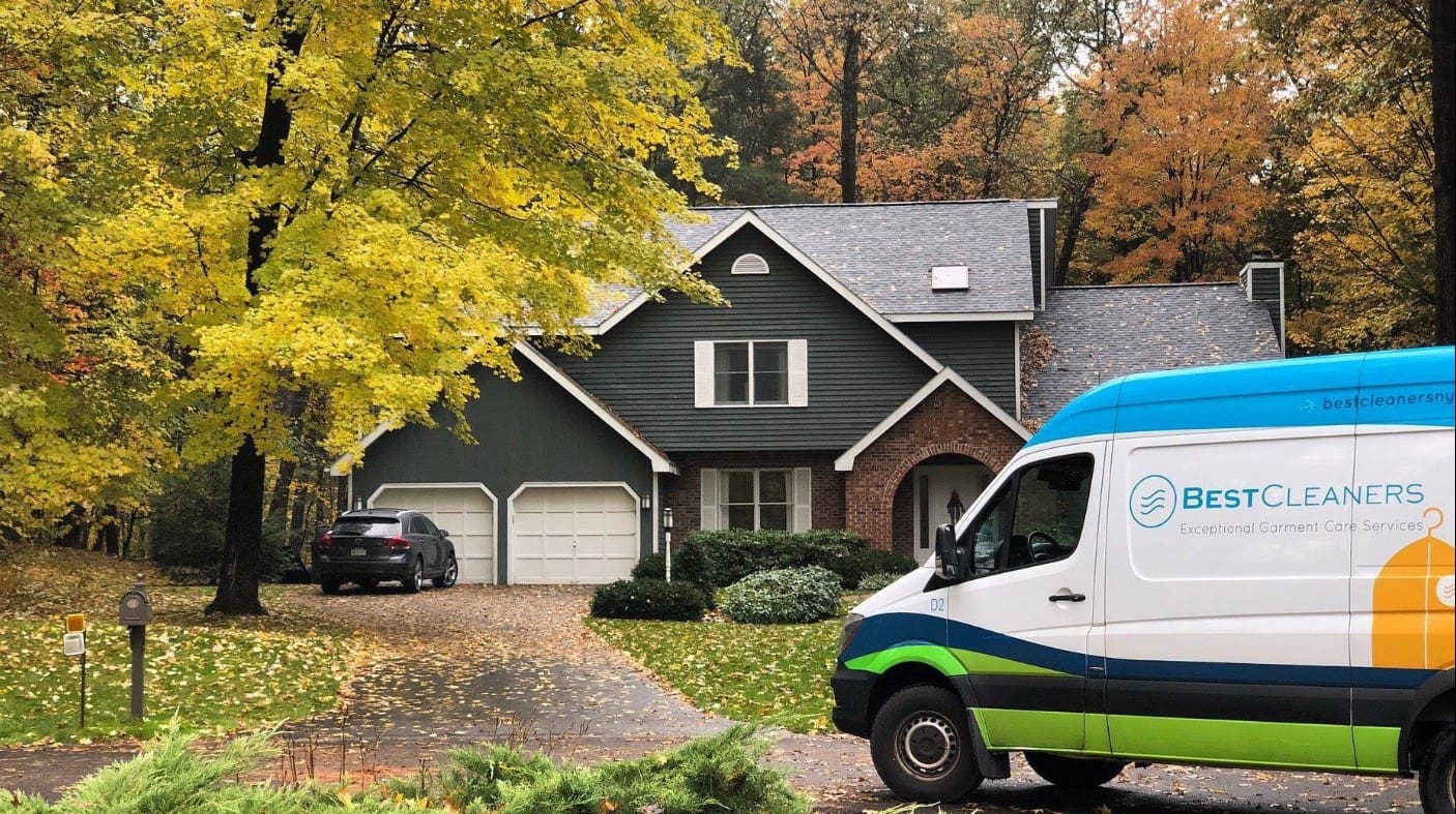 Best Cleaners delivery van parked in front of a residential home surrounded by autumn foliage, showcasing their exceptional garment care services and free pickup and delivery options.