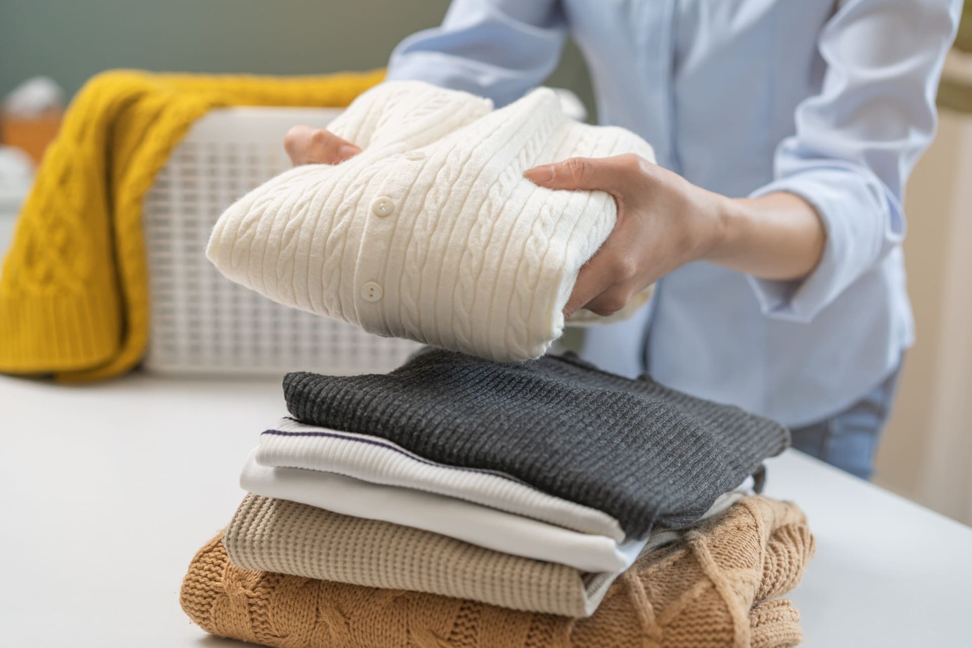 Person folding freshly laundered sweaters, showcasing neatly stacked clean clothes, emphasizing Best Cleaners' Wash and Fold Laundry Service.