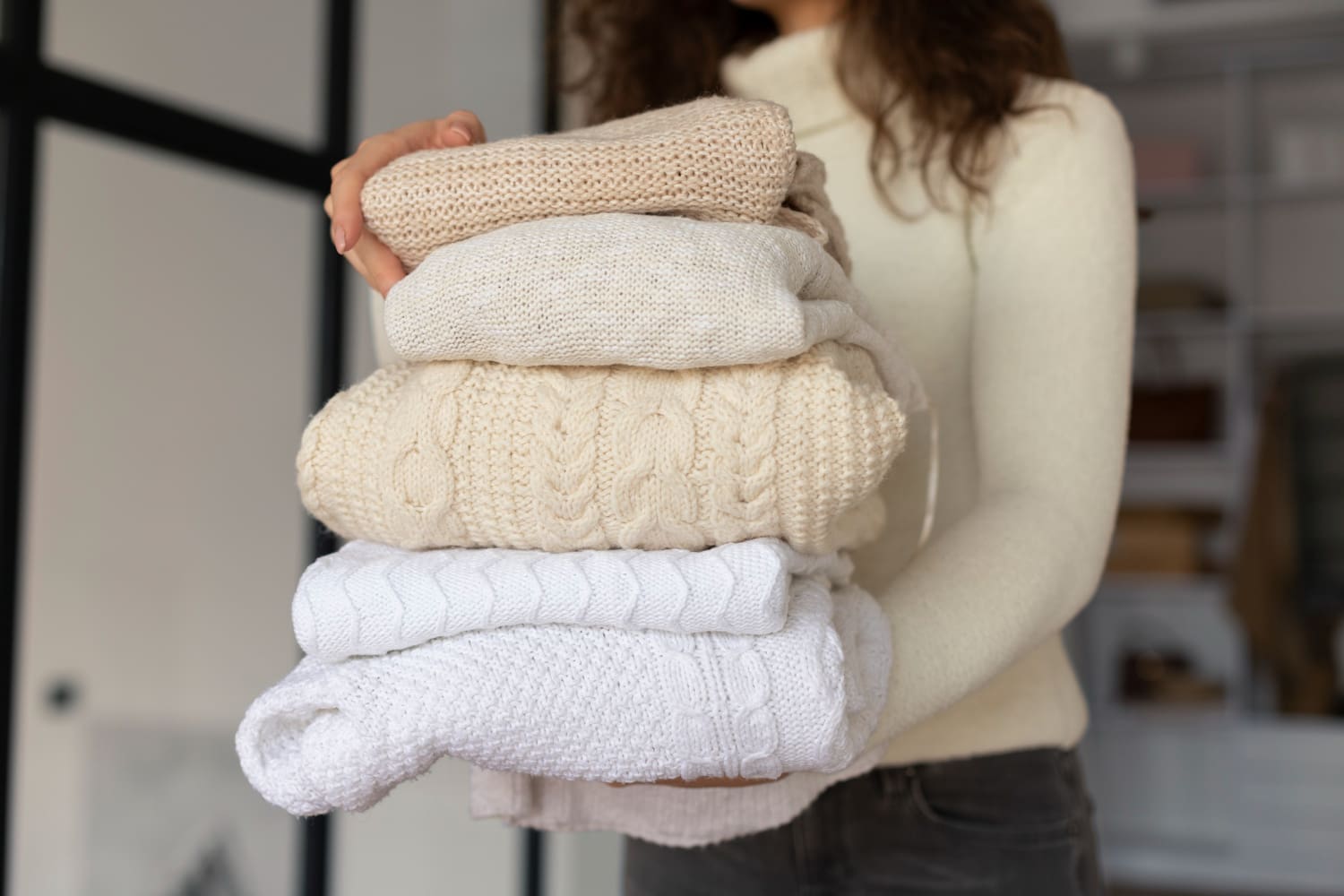 Person holding neatly folded sweaters in neutral colors, showcasing the quality of laundry services and emphasizing professional wash and fold capabilities.