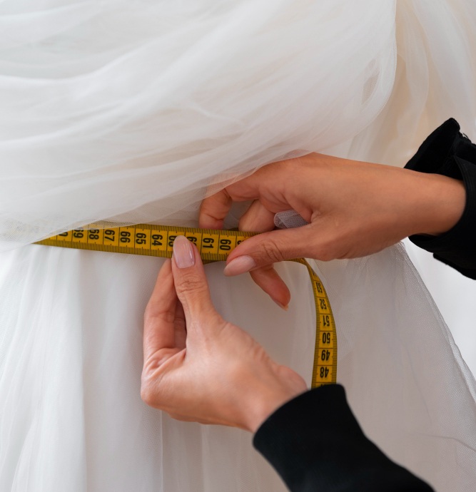Close-up of hands measuring the waist of a white dress with a yellow measuring tape.