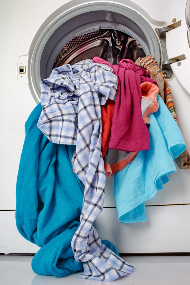 A washing machine with its door open and various colorful clothes spilling out.